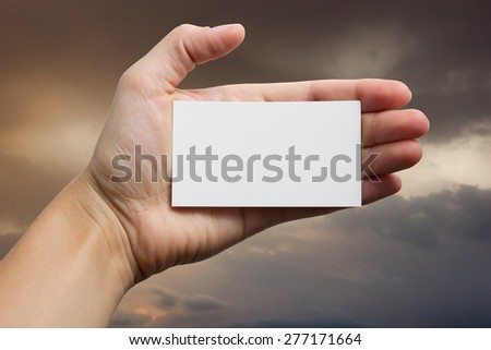 Hands holding a white business visit card, gift, ticket, pass, present closeup on sky background. Copy space.