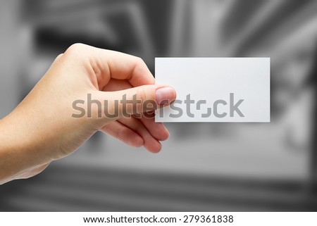 Hands holding a white business visit card, gift, ticket, pass, present close up on blurred blue background. Copy space