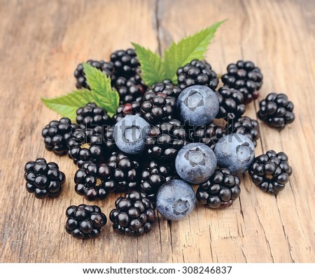 Sweet berries go blueberries and blackberries on wooden texture.