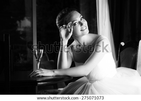 Beautiful blonde bride seats near table, is ready for a new bright life, inside interior. White Wedding dress. Pretty young woman love. Black and white photo.