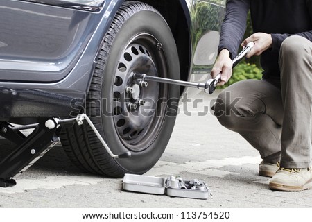 Woman is changing  tire with wheel wrench.