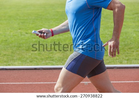 Runner checks his fitness data on a smartphone while running before uploading it to the cloud. He wears a fitness tracker wristband on the right arm. Unfiltered version