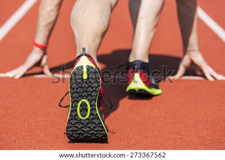 Runner in a stadium in start position with hands on the line. Unfiltered version.