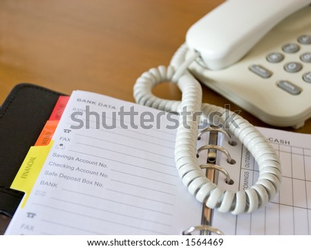 Close-up of a home phone and an open personal planner showing banking pages