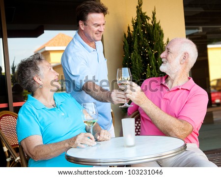 Waiter serving wine to a senior couple at a restaurant.