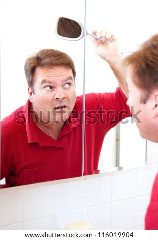 Mature man in his forties uses a mirror to check for bald patches in his hair.
