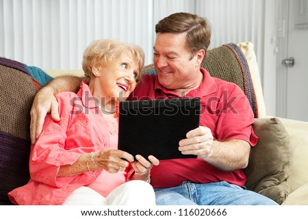 Adult son teaching his elderly mother how to use her new tablet PC.