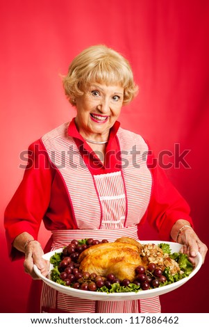 Sweet retro grandmother holding a Christmas or Thanksgiving holiday turkey dinner.  Red background.
