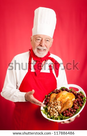 Handsome, experienced chef holding stuffed turkey dinner.  Red background.
