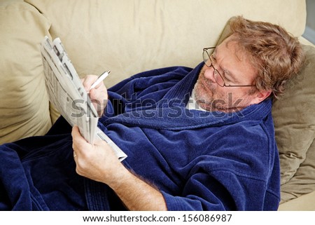 Unemployed man checking the classified section of the newspaper for job opportunities.  Could also be doing crossword puzzle