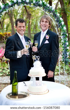 Handsome gay couple toasting with champagne at their beautiful outdoor wedding reception.
