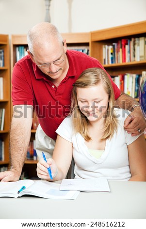 Father or teacher helping a teenage student at the library.