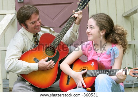 A father and daughter playing guitars together and laughing.