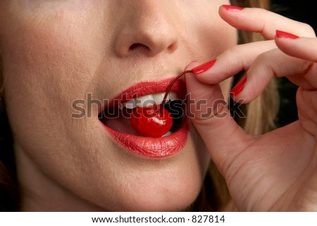 A closeup of red lips and white teeth biting into a bright red cherry.