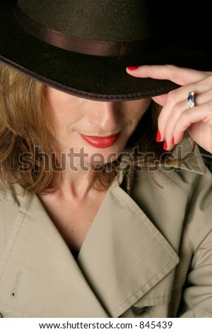 A beautiful, sexy woman in a trench-coat and fedora hat.  Her eyes are concealed beneath the brim of the hat.