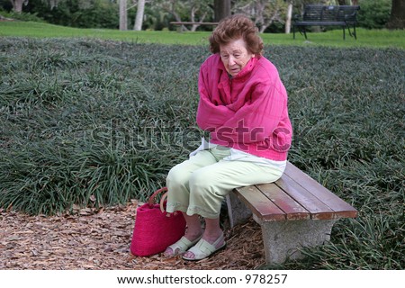 A senior woman shivering in the cold, alone on a park bench.
