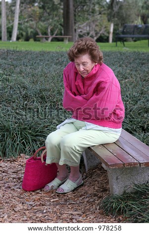 A  senior citizen shivering in the cold on a park bench.