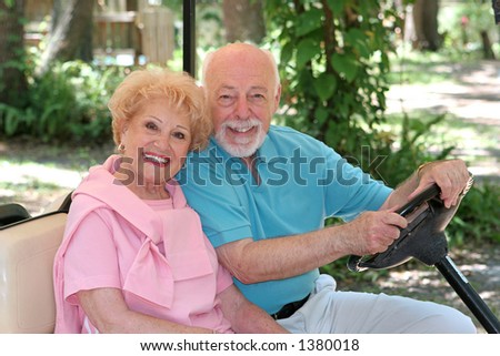 A happy senior couple driving a golf cart through a resort.
