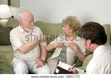 A senior couple seeking marriage counseling.  He\'s pointing at her and she\'s looking surprised.  Focus on husband.