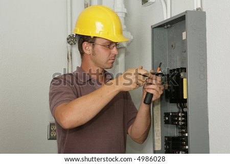 An electrician working on an industrial breaker panel.  Model is an actual electrician performing all work to industry codes and safety standards.
