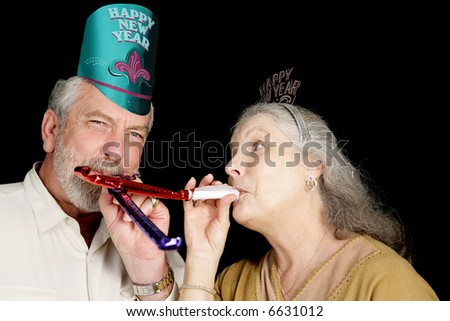 Mature couple in New Years party hats blowing noise-makers.  Isolated on black.