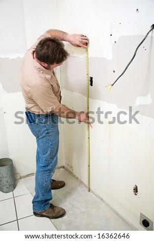Construction worker measuring the wall during a kitchen remodeling job.  Authentic and accurate content depiction.