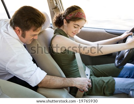 Driving instructor or father encouraging a teen driver to use her seatbelt.