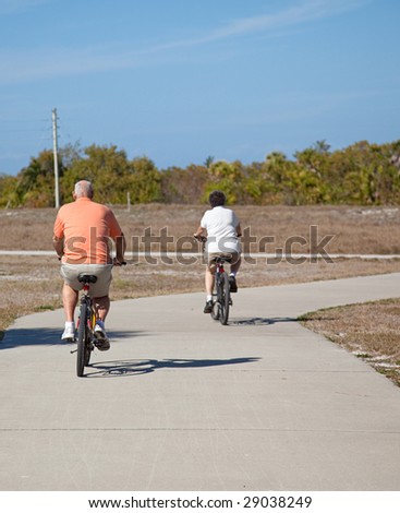 Rear view of a senior couple riding their bicycles.  Focus on the husband, in the foreground.