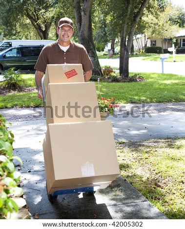 Delivery man or mover pushing a dolly loaded with boxes up the front walk.
