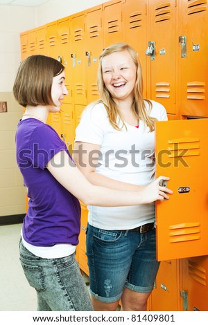 Two teenage girls talking by the lockers in the hallway of their high school.