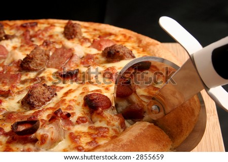 Pizza cutter slicing through a meat lovers deep pan