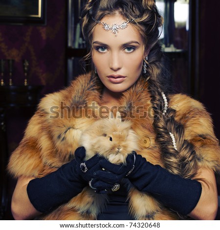 Attractive glamorous woman in fox fur coat with rabbit in her hand.