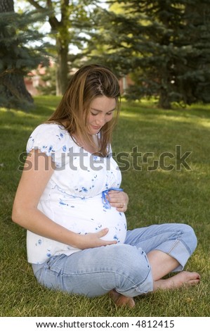 Happy pregnant woman holding her belly, sitting in the park.
