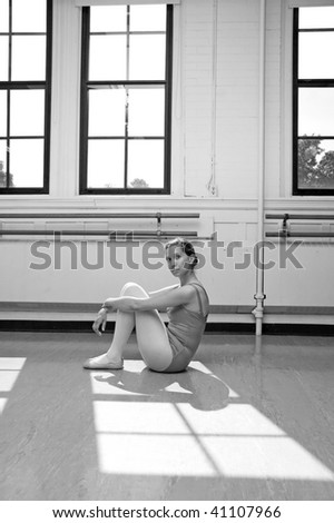 Ballerina sitting on the floor in a sunlit studio.