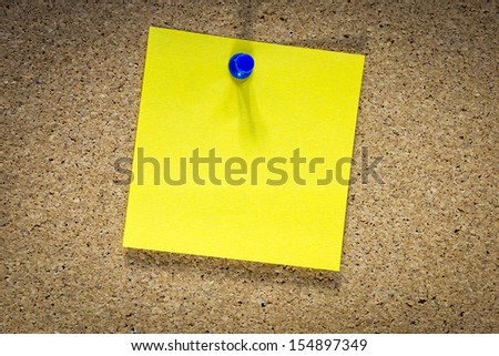 Blank yellow sticky note pined on a cork bulletin board.