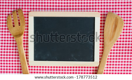 Menu blackboard with wooden spoon and fork on a red checkered table cloth