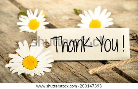 Flowers and label with lettering thanks on wooden background
