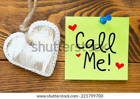 Yellow small sticky note on an wooden table with biscuit heart cookie . Call me!