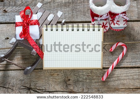 Notebook and Christmas decorations on wooden background. Sled, boots, candy, gift, star,