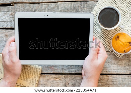 Man holding white tablet. Male hand holding white tablet. Workspace with coffee cup and muffin on old wooden table