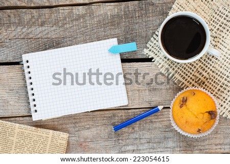 Notebook with a sticker. Notebook checkered with blue sticker on wooden desk with cup of coffee and muffin
