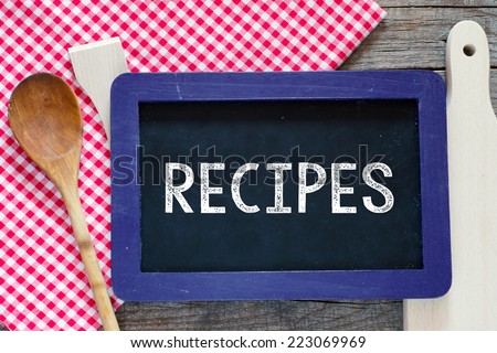 Chalked Recipes word on blackboard. Chalked word Recipes on blackboard with wooden spoon and fork on a red checkered table cloth