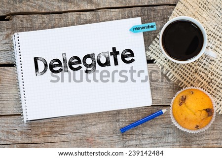 Notebook with delegate sign. Notebook with delegate sign and sticker remember on wooden desk with cup of coffee and muffin