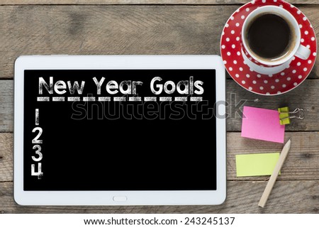 New year goals and computer. Tablet computer with stickers,cup of coffee and New year goals on the wooden table
