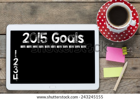 New year goals 2015. Tablet computer with stickers,cup of coffee and New year goals 2015 on the wooden table