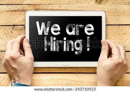 We are hiring On PC. Hands with Tablet PC with we are hiring text on wooden background
