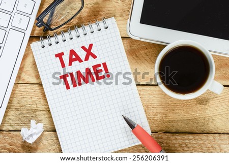 Notebook with tax time. Workplace with keyboard , tablet pc , coffee, notebook with tax time and pen on wood table