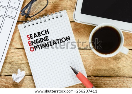 Notebook with search engine optimization. Workplace with keyboard , tablet pc , coffee, notebook with search engine optimization and pen on wood table