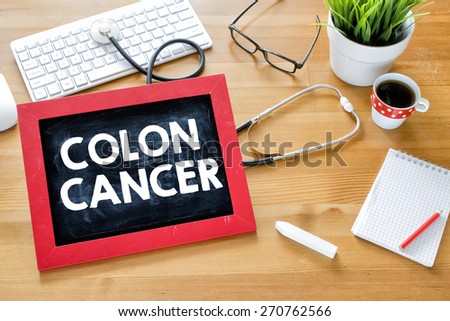 Handwritten colon cancer on blackboard. Handwritten colon cancer with chalk on blackboard,stethoscope, keyboard,notebook,glasses,cup of coffee and green plant on wooden background