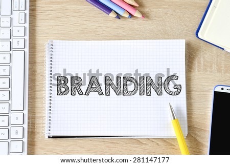 Notepad with branding, keyboard,mobile phone and pencils on wooden background